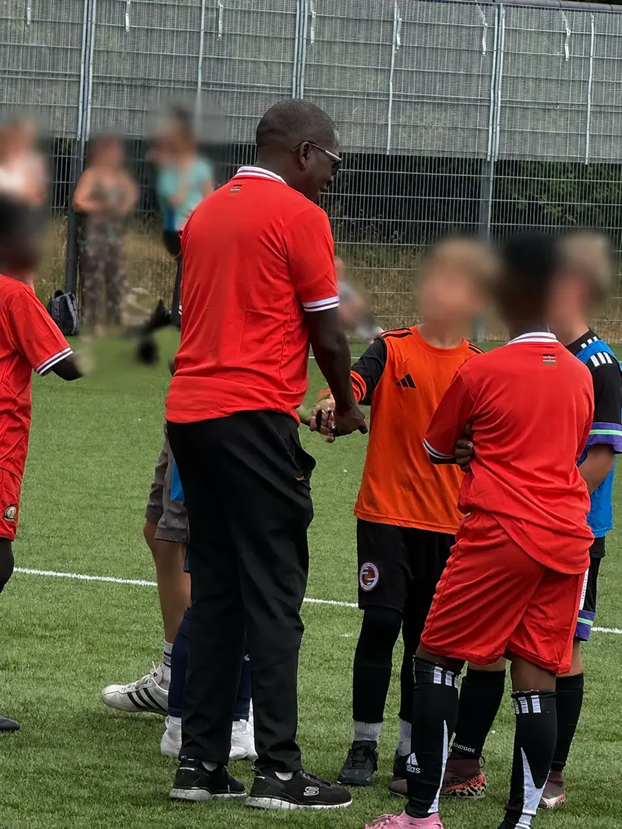 A coach greeting young football players during a friendly tournament